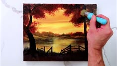 a man is painting a sunset scene with water and trees on the side of the wall