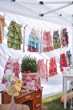 there are many dresses hanging on the clothesline outside in the tent, and one has a potted plant next to it