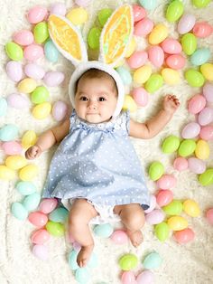 a baby wearing an easter bunny costume laying on some colored eggs in front of her