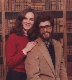 a man and woman standing next to each other in front of bookshelves with their arms around each other