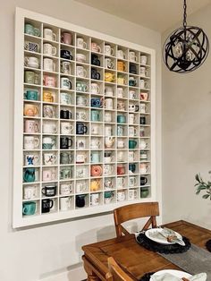 a dining room table with plates and cups on the wall behind it, next to a potted plant