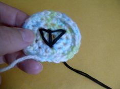 a hand holding a crocheted object with a black triangle on it's side