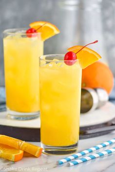 two glasses filled with orange juice and garnished with cherries on the rim