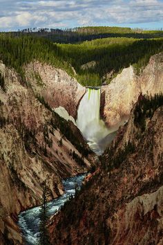 a waterfall in the middle of mountains with snow on it's sides and trees around