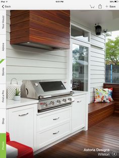 an outdoor kitchen with wood flooring and white cabinets on the side of a house