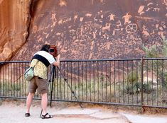 a person taking pictures with their camera in front of a large rock painting on the side of a mountain