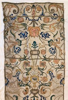 an old embroidered cloth with flowers and vines on the side, hanging from a wall