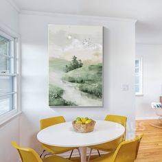 a white table with four yellow chairs in front of a large painting on the wall