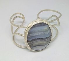 This is a 30 x 40mm blue lace agate cabochon set in .925 sterling silver (embellished bezel set) on a 3 wire cuff. approx. dimensions 5.50" around wrist 1.75" width at stone Adjustable Oval Sterling Silver Cuff Bracelet, Silver Sterling Silver Cuff Bracelet With Cabochon, Adjustable Cabochon Sterling Silver Cuff Bracelet, Adjustable Sterling Silver Cuff Bracelet With Cabochon, Adjustable Sterling Silver Cabochon Cuff Bracelet, Silver Agate Bangle Cuff Bracelet, Adjustable Oval Agate Jewelry, Silver Agate Gemstone Cuff Bracelet, Unique Silver Agate Cuff Bracelet