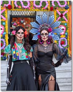 two women dressed up in costumes and headpieces posing for the camera with colorful flowers behind them