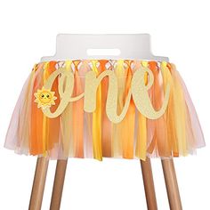 an orange and yellow birthday decoration with the word one on it's front, sitting on wooden legs