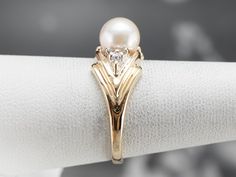 This vintage pearl ring has a sleek chevron design crafted from yellow gold. The polished gold frames the pearl beautifully, which has a gorgeous creamy white luster with hints of gray undertones. This single pearl is accented by a trio of sparkling diamonds making this the perfect piece to gift for a variety of occasions! Metal: 14K Yellow Gold Gem: Pearl Gem Measurements: 6.7 mm, Round Accents: 6 Diamonds totaling .04 Carats, H in Color, I1 in Clarity Ring Size: 6.50 Marks: "14K A" Stamped on Classic Pearl Ring With Single Diamond For Anniversary, Classic Pearl White Diamond Ring For Formal Occasions, Classic Pearl Diamond Ring With Accents, Classic Pearl Diamond Ring With Diamond Accents, Elegant Gold Pearl Ring With Diamond Accents, Elegant Diamond Ring With Pearl Drop For Anniversary, Elegant Pearl Drop Diamond Ring For Anniversary, Classic Yellow Gold Pearl Ring With Single Diamond, Classic Yellow Gold Pearl Ring With Diamond