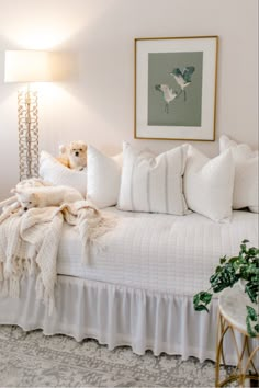 a white bed with pillows and blankets on top of it next to a table lamp