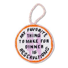 a cross stitch ornament with an orange and pink ribbon hanging from it's center