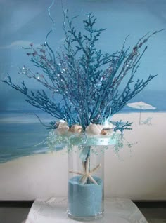 a glass vase filled with blue flowers and seashells on top of a table