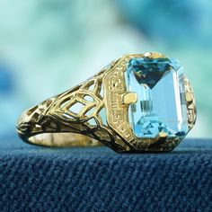 Embrace timeless elegance with this stunning ring, showcasing a classic vintage style with yellow gold intricate filigree work. The delicate design exudes sophistication, making it a truly captivating piece. The emerald-cut blue topaz is set high, emphasizing its size and brilliance, allowing maximum light to enhance its color and sparkle. This exquisite ring is a perfect blend of vintage charm and modern allure, making it an irresistible addition to your collection. CHARACTERISTICS Status: Made Vintage Topaz Ring, Cocktail Ring Designs, Oc Outfits, Classic Vintage Style, Topaz Color, Delicate Design, Filigree Ring, Topaz Ring, Cocktail Ring