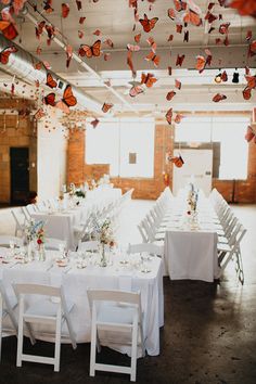 a room filled with lots of tables covered in white cloths and butterfly decorations hanging from the ceiling