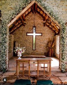 the inside of a church with a cross and flowers on the alter, surrounded by greenery