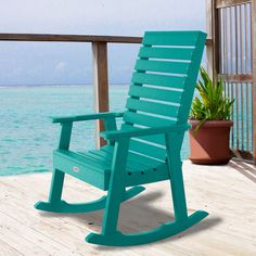 a green rocking chair sitting on top of a wooden deck next to the ocean with potted plants