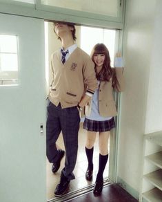 a man and woman standing next to each other in front of a door wearing school uniforms