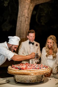 a man cutting into a pizza on top of a table next to two other people