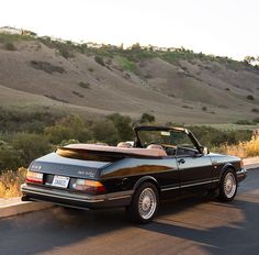 a black convertible car parked on the side of the road in front of some hills