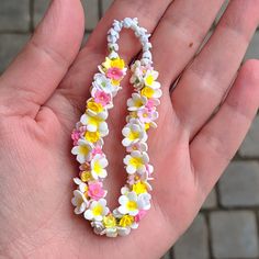 a hand is holding a flowered necklace on it's palm with bricks in the background