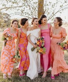 a group of women standing next to each other wearing dresses and holding bouquets in their hands