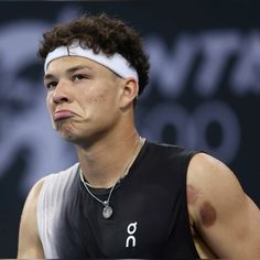 a male tennis player wearing a black shirt and white headband with brown spots on his face