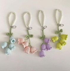 four crocheted keychains with bows and pearls hanging from each side on a white surface