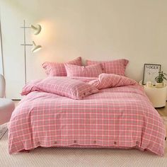 a bed with pink plaid sheets and pillows in a room next to a white chair