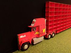 a red toy truck is parked next to a black wall with shelves on the side