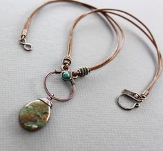 a close up of a necklace on a white surface with a brown cord and two charms