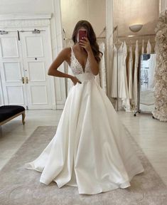 a woman standing in front of a mirror wearing a white wedding dress and holding her hand to her face