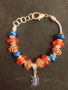 a bracelet with orange and blue beads, silver charms and a detroit tigers charm on it