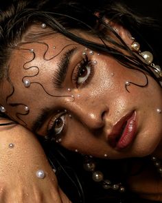 a woman with her hands on her head and face covered in beads, pearls and jewels