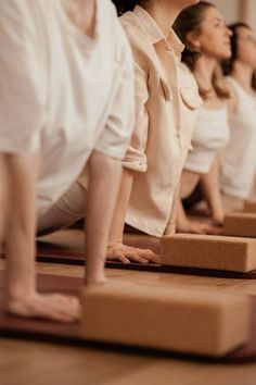 a row of women in white shirts are doing yoga on wooden blocks with their feet up