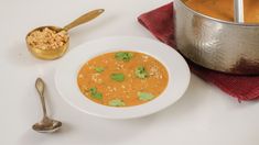 a white bowl filled with soup next to a spoon and a pot full of food