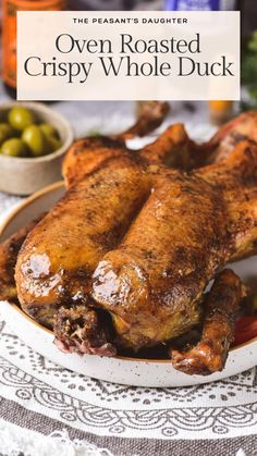 an oven roasted crispy whole duck on a white plate with green olives in the background