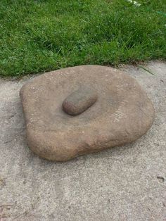 a rock sitting on top of a cement slab in the middle of a grass covered field