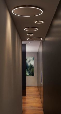 an empty hallway with wooden flooring and circular lights on the ceiling, leading to another room