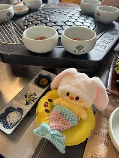 a small stuffed animal sitting on top of a plate next to bowls and spoons