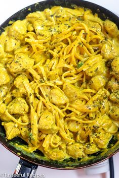 a skillet filled with pasta and chicken in yellow sauce on top of a stove