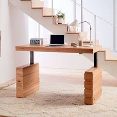 a laptop computer sitting on top of a wooden desk in front of a stair case