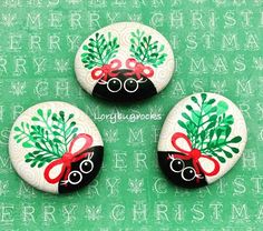 three decorated rocks sitting on top of a green surface with christmas decorations painted on them