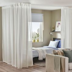 a living room filled with furniture and a large window covered in curtains next to a bed