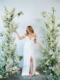 a woman wearing a white dress standing in front of flowers