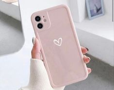 a woman holding up a pink phone case with a heart sticker on it