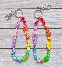 two key chains with different colored beads and charms attached to them on a wooden surface