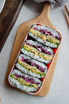 a tray filled with assorted sushi on top of a wooden cutting board